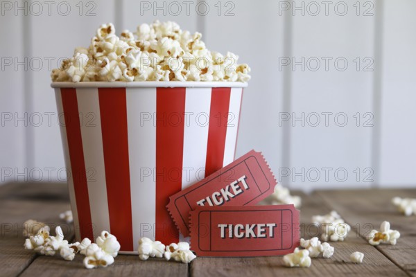 Red and white striped popcorn bucket with antique red movie tickets on rustic wooden table.