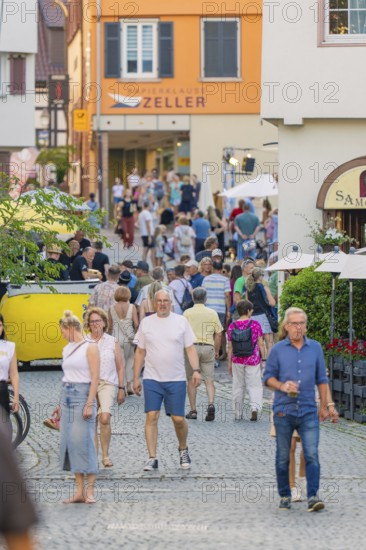 People stroll through a lively old town street, surrounded by shops and summery impressions, 950