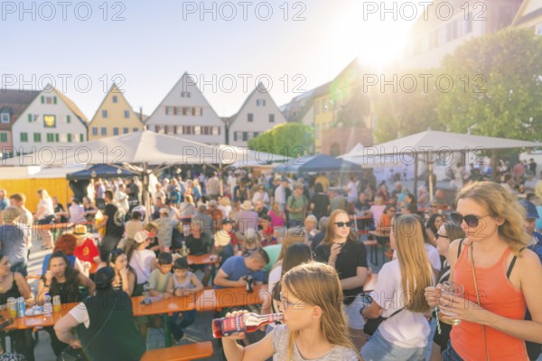 Visitors relax at tables in sunny weather, surrounded by historic house facades, 950 years Weil der