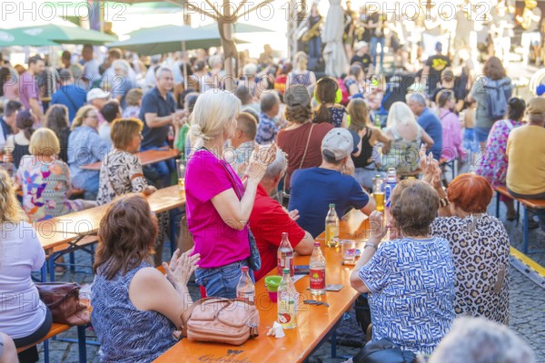 People sitting at long tables at a party, applauding and enjoying drinks, 950 years Weil der Stadt