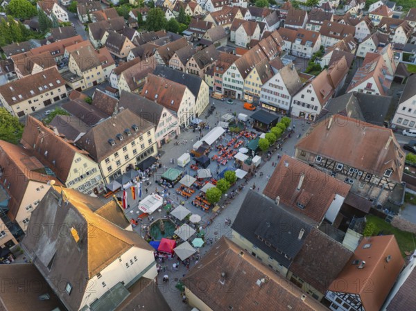 Lively town festival with numerous visitors and green trees surrounded by buildings seen from the