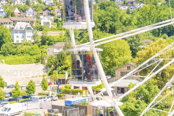 Detail of a Ferris wheel with passengers, surrounded by green trees and urban surroundings, Calw,