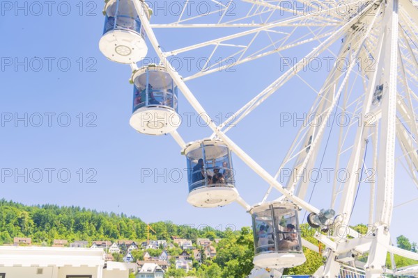 Ferris wheel with cabins in front of a blue sky, green trees and houses in the background, Calw,