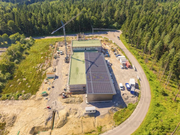 Aerial view of a construction site with solar panels, surrounded by woodland and a crane, new fire
