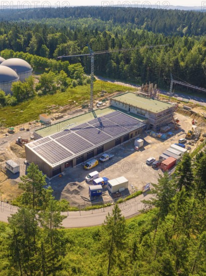 Aerial view of a construction site with solar panels and a crane, surrounded by dense forest and