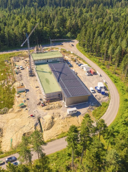 Building with solar roof in a construction site surrounded by forest, crane nearby, various