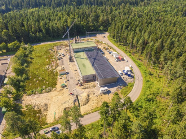 Solar roof building on a construction site surrounded by trees, crane and vehicles visible, aerial
