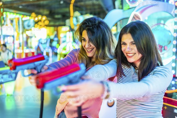 Two young women enjoying leisure time, playfully engaging with toy guns in a vibrant amusement