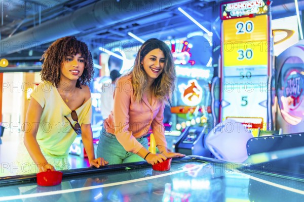 Two young women enjoying a friendly game of air hockey in a vibrant arcade, illuminated by colorful