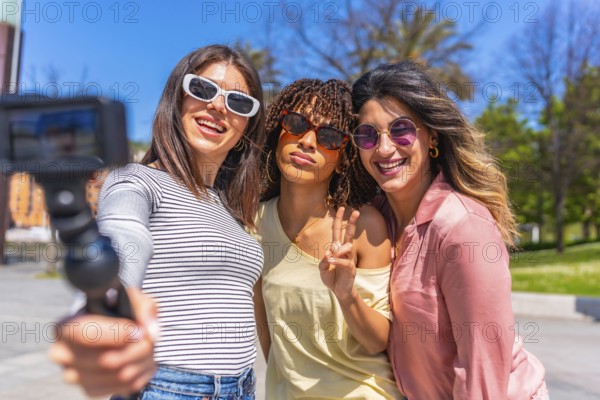 Three joyful women enjoying a sunny day, taking a selfie with an action camera while bonding during