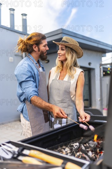 Happy couple enjoying a sunny summer day, grilling marshmallows on a rooftop barbecue, sharing
