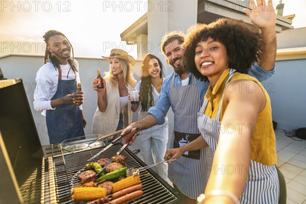 Cheerful multi ethnic friends are grilling meat and vegetables, drinking beer and taking a selfie