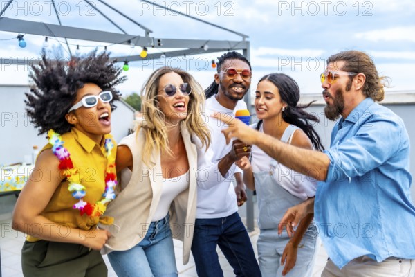 Cheerful multi ethnic friends enjoying a vibrant rooftop party, singing karaoke, dancing, and