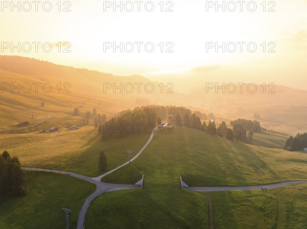 Wide, green hills under bright evening light with scattered mountain huts, Alpe di Siusi,
