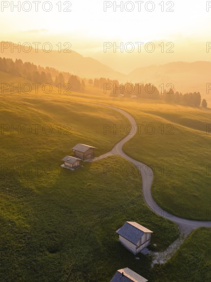 Mountain huts on gentle hills with scattered groups of trees in the light of the sunset, Alpe di