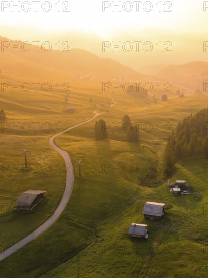 Undulating hills and forests in sunset mood with scattered mountain huts, Alpe di Siusi, Dolomites,