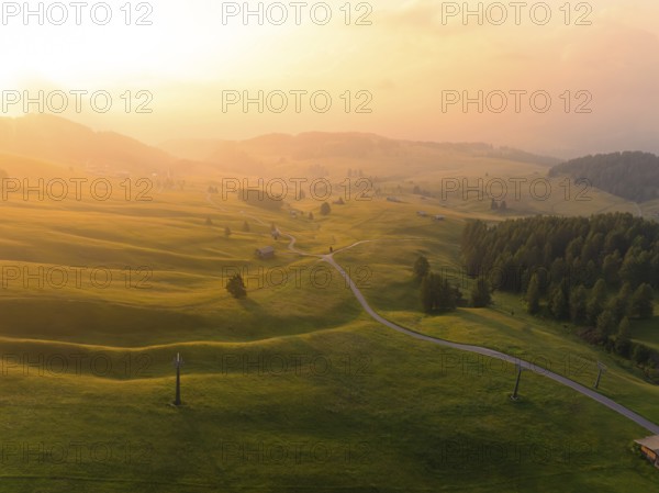 Soft hills and meadows in the golden light of sunset with scattered mountain huts, Alpe di Siusi,