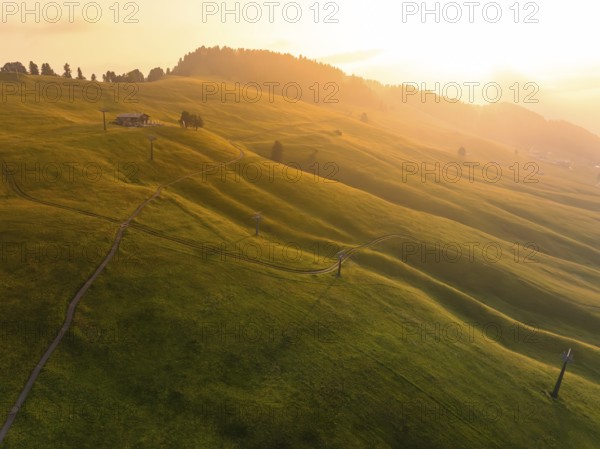 Green, gentle hills in warm light with paths and a secluded building, Alpe di Siusi, Dolomites,