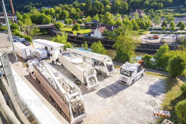 Several trucks and trailers on a car park, surrounded by green landscape and a river, Ferris wheel