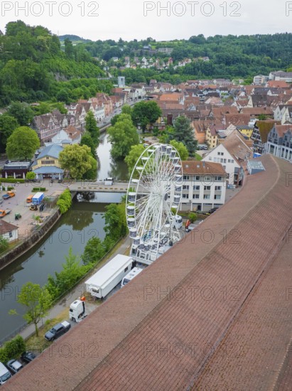 View of a Ferris wheel in an urban area with a river and hilly, green surroundings, construction of