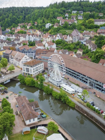 Aerial view of an idyllic village with a Ferris wheel by the river and surrounded by green hills,