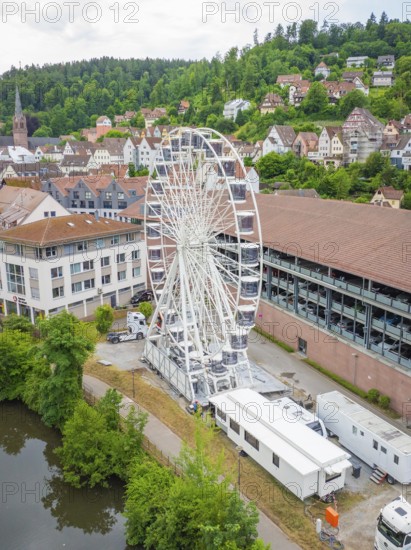 The Ferris wheel stands prominently in an urban landscape with a river and wooded hills, Ferris