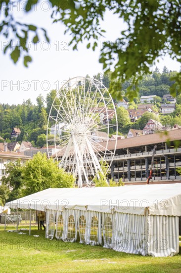 Ferris wheel behind a large white tent, surrounded by village houses and green hills, Ferris wheel