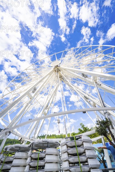 Partially erected Ferris wheel in front of a clear blue sky with cloud formations, Ferris wheel