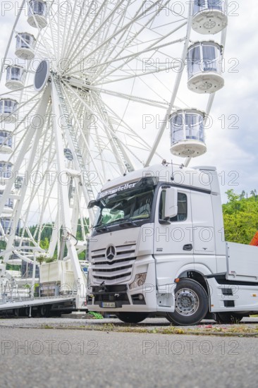 Large Ferris wheel in the background of a parked white lorry on a cloudy day, Ferris wheel