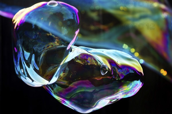 Irregular, iridescent soap bubble in the colours of the rainbow against a black background,