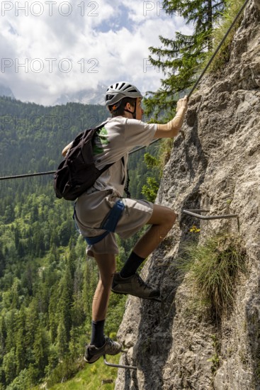 Mountaineer climbing over a steep ladder in the Isidor via ferrata, Grünstein, Schönau am