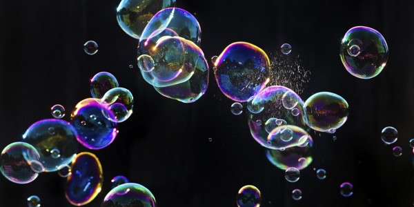 Iridescent soap bubbles with a just burst bubble in front of a black background, Recklinghausen,