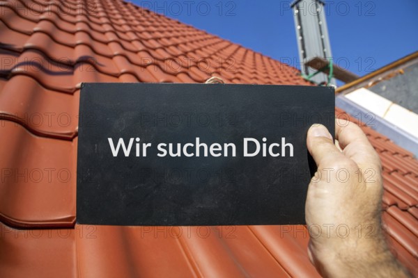 Employee search roofer: Man holding a sign (with added text) WE ARE LOOKING FOR YOU in front of a