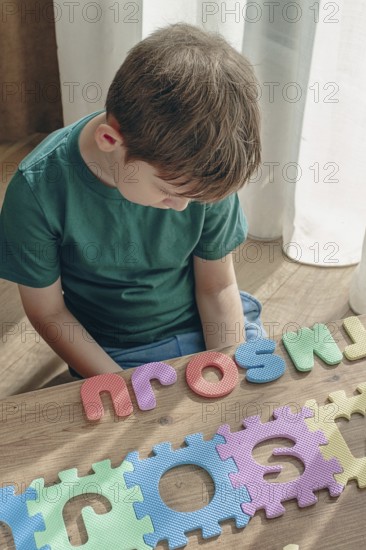 Boy with autism, expresses frustration, playing with puzzle pieces, on a wooden table, natural