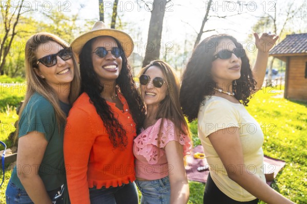 Four diverse women wearing stylish sunglasses and sharing joyful smiles while relaxing together in