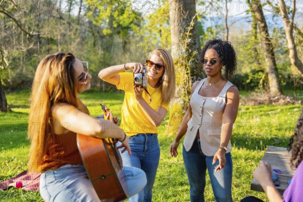 Group of friends soaking up the sun in nature, playing music, capturing moments with cameras, and