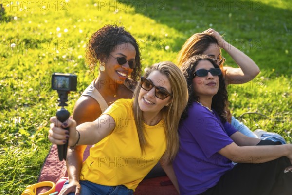 Four cheerful female friends are recording a video blog in the park using an action camera,