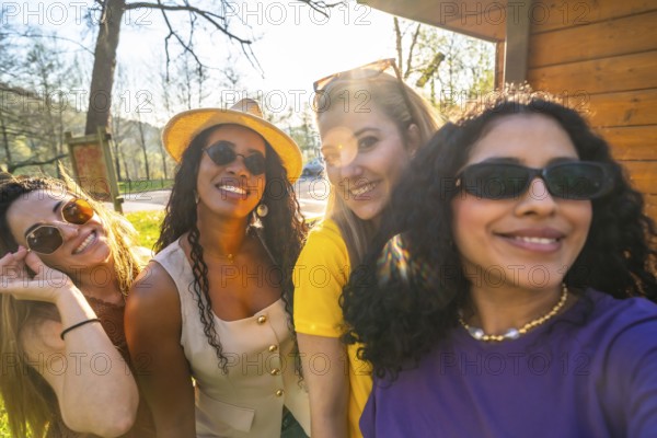 Four cheerful women enjoying a sunny day in the park, smiling and capturing memories together while