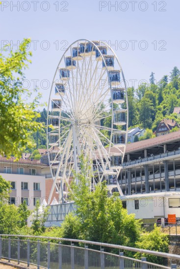 A white Ferris wheel in daylight against a backdrop of buildings and wooded hills, 950 years of