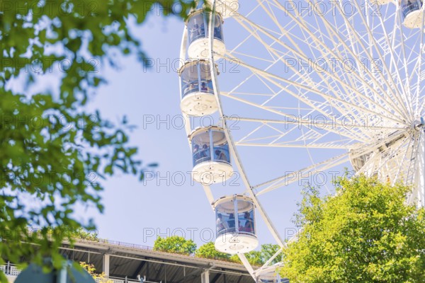 Close-up of a Ferris wheel with cabins, visible between green trees and a blue sky, 950 years Calw,