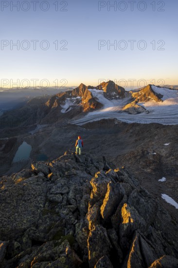Mountaineer in front of picturesque high mountain landscape at sunrise with alpenglow, glacier and