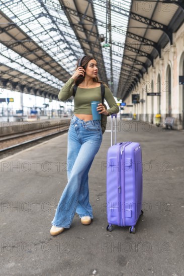 Stylish tourist listening to music while waiting for her train at a station platform, enjoying a