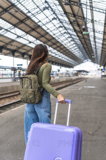 Tourist wearing headphones and carrying luggage strolls through a bustling train station, embracing