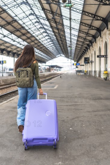 Tourist walking along a train platform, pulling a trolley suitcase while embarking on an exciting