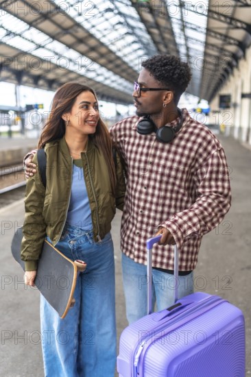 Happy multi ethnic couple walking together on platform while waiting for train, embracing and