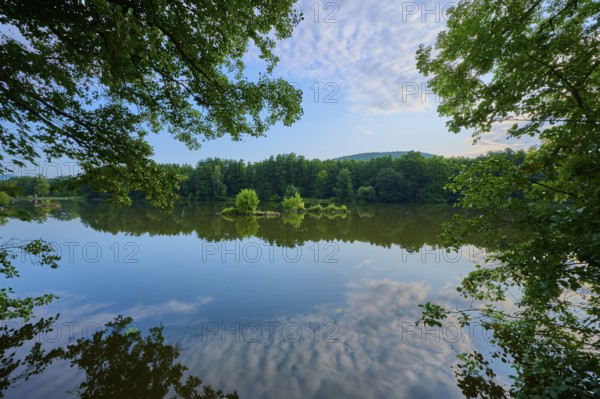 A calm, reflecting river surrounded by trees and small islands in the morning light, summer,