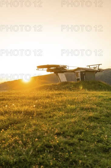 Sunset over a green meadow with a silhouette of a cable car station, Alpe di Siusi, Dolomites,