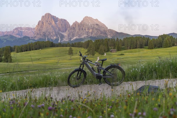 A bicycle stands on a gravel road with a view of the nearby Dolomites, Sassolungo Group, Alpe di
