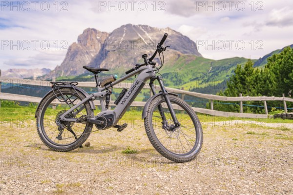 Grey e-bike on a stony path with mountain view and wooden fence in the background, Alpe di Siusi,