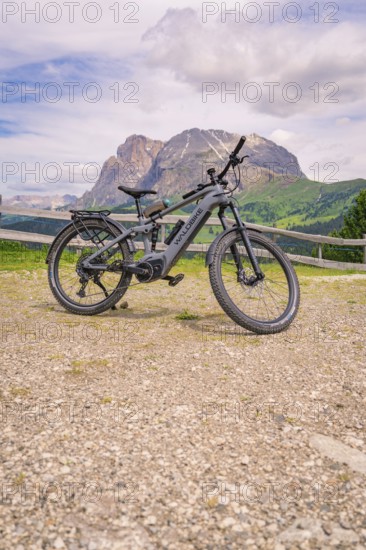An e-bike stands on a gravel path in front of a mountain landscape, Alpe di Siusi, Dolomites, South